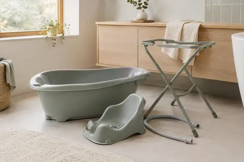 Baignoire bébé grise avec siège, support métallique et tuyau de vidange dans une salle de bain lumineuse