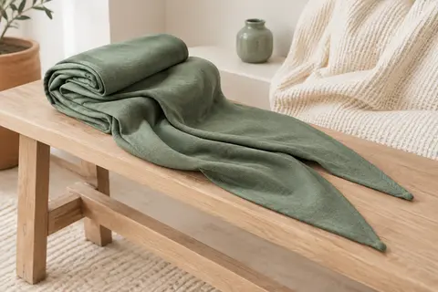 Écharpe de portage verte en coton extensible, pliée sur un banc en bois clair dans une pièce lumineuse.